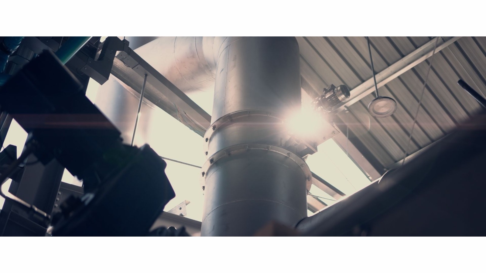Steel piping and machinery inside Enable Earth's pyrolysis facility at Wiang Pa Pao, sunlight breaking through the plant hall